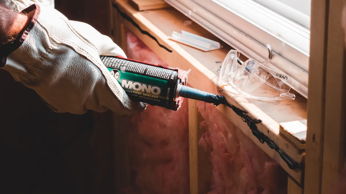 Attic insulation installation: what homeowners should know Worker sealing gaps around attic insulation with caulk
