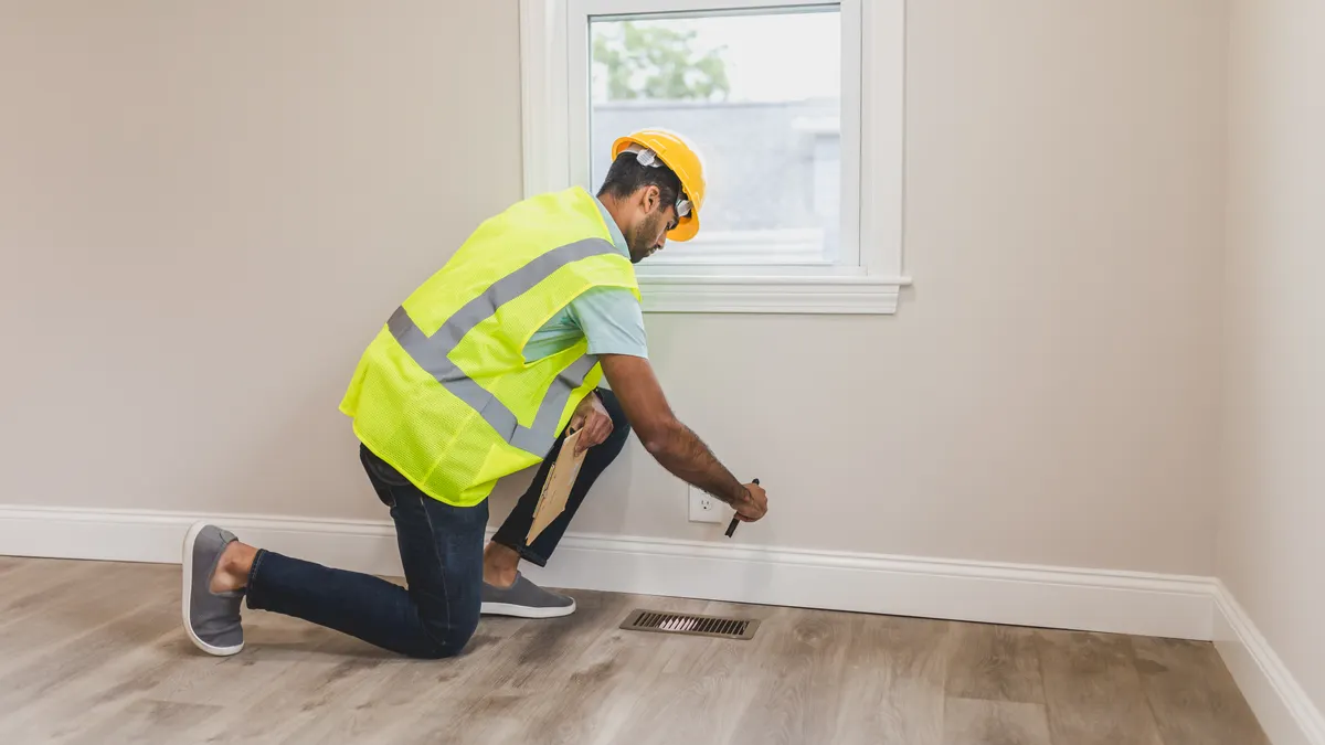 DIY home energy audit checklist Worker inspecting a floor vent in an empty room
